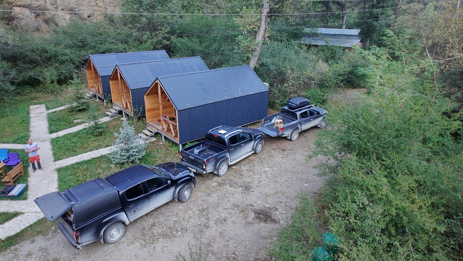 Aerial view of three BUL expedition pickups beside wooden guest cabins