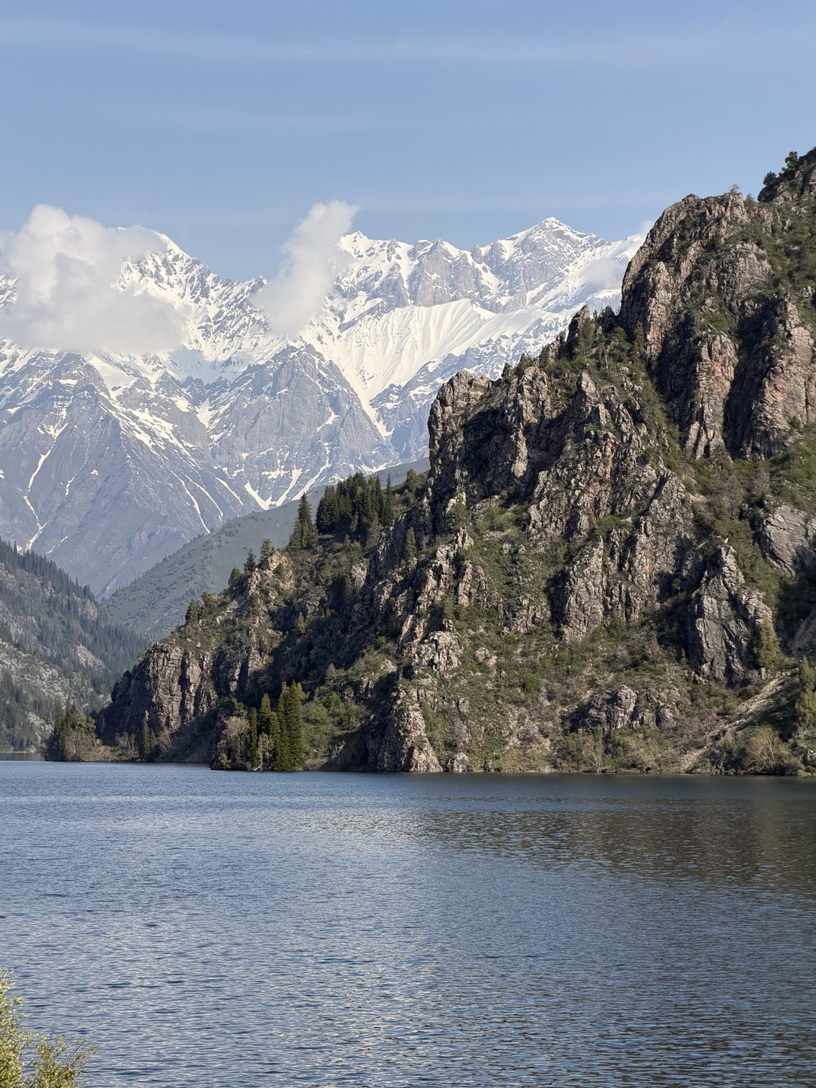 Mountain lake with rocky shores, forest and snow-covered peaks